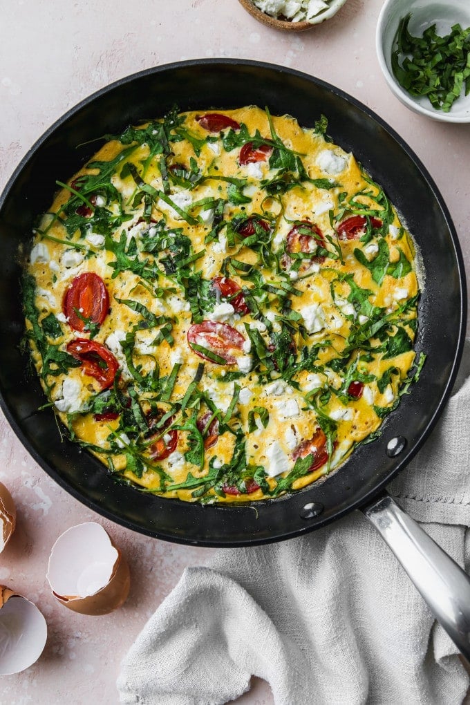 Overhead photo of an arugula and tomato frittata in a skillet.