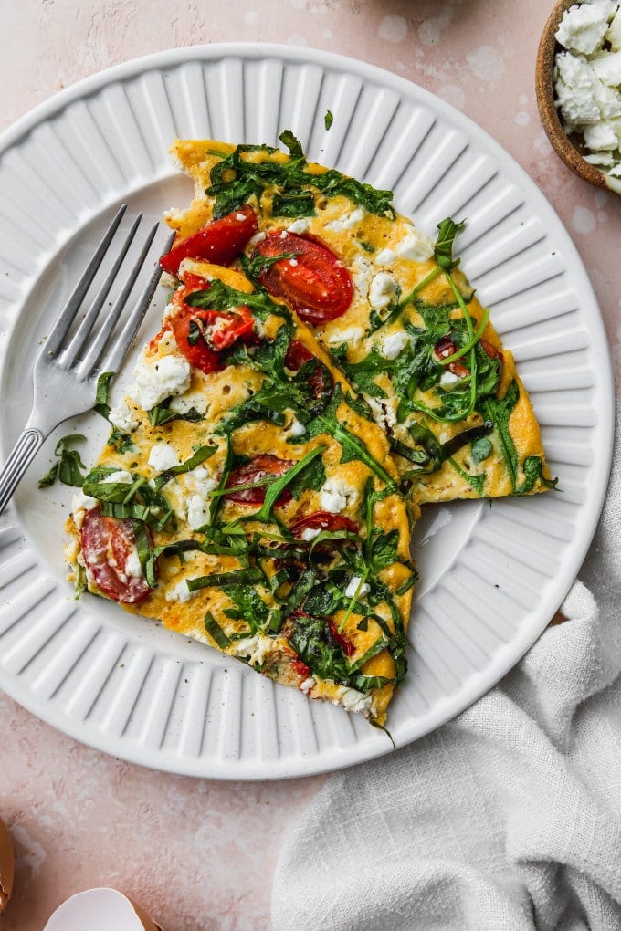 Overhead photo of a serving of arugula and tomato frittata on a white plate.