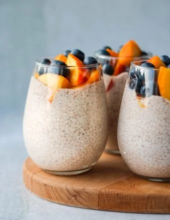 3 chia seed puddings topped with peaches and blueberries in glass jar
