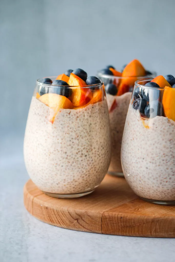 3 chia seed puddings topped with peaches and blueberries in glass jar
