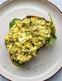white plate with mashed avocado egg salad sandwich over a slice of toast