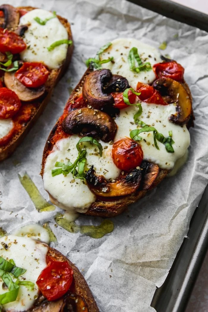 Side angle photo of a sourdough pizza toast topped with melted bocconcini, tomatoes, and mushrooms straight out of the oven.