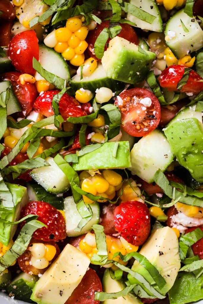 close up shot of summer salad with corn, tomato, avocado, strawberry, basil, feta
