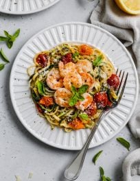 overhead photo of white plate topped with spaghetti pasta, zoodles, tomatoes, spinach, and garlic prawns