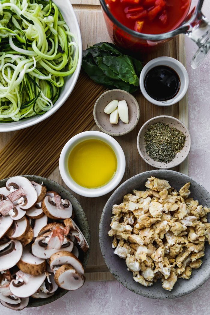 overhead photo of wood cutting bowl with bowls of ingredients on top to make a vegan pasta recipe
