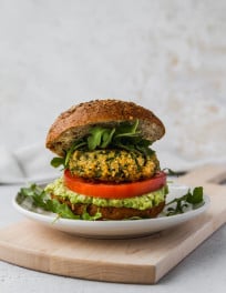 Straight on photo of a salmon quinoa burger in a bun on a white plate and wooden cutting board.