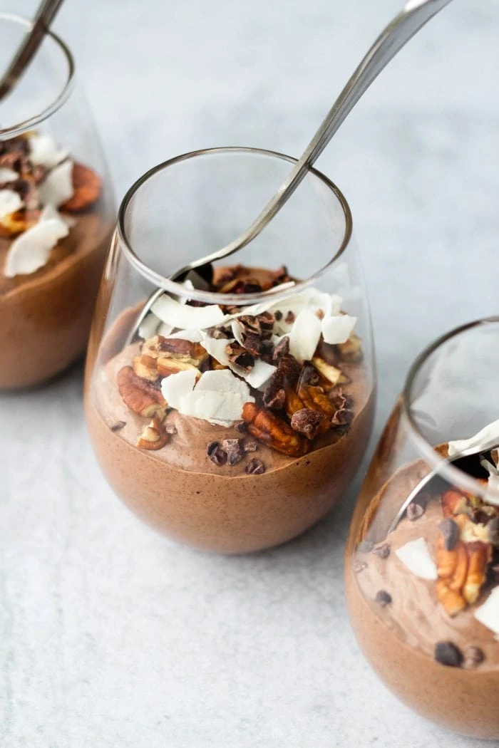 3 glass jars of blended chocolate ginger chia pudding topped with nuts and coconut flakes