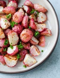 Oven-roasted radishes in a white bowl with chopped parsley
