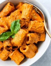 rigatoni pasta with roasted red pepper cashew cream sauce and basil in a white bowl