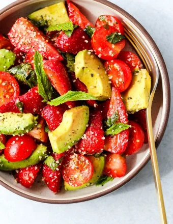 strawberry tomato avocado salad with mint, basil, balsamic, and hemp seeds in a white and brown bowl