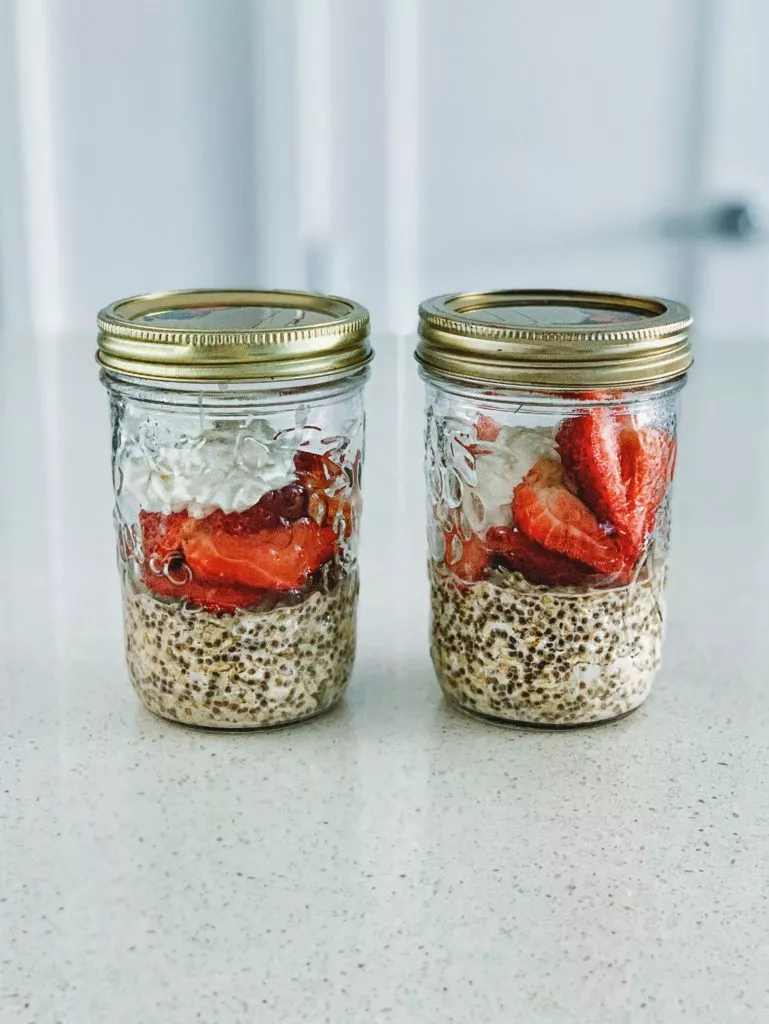 Two glass mason jars with overnight steel cut oatmeal, strawberries, and greek yogurt