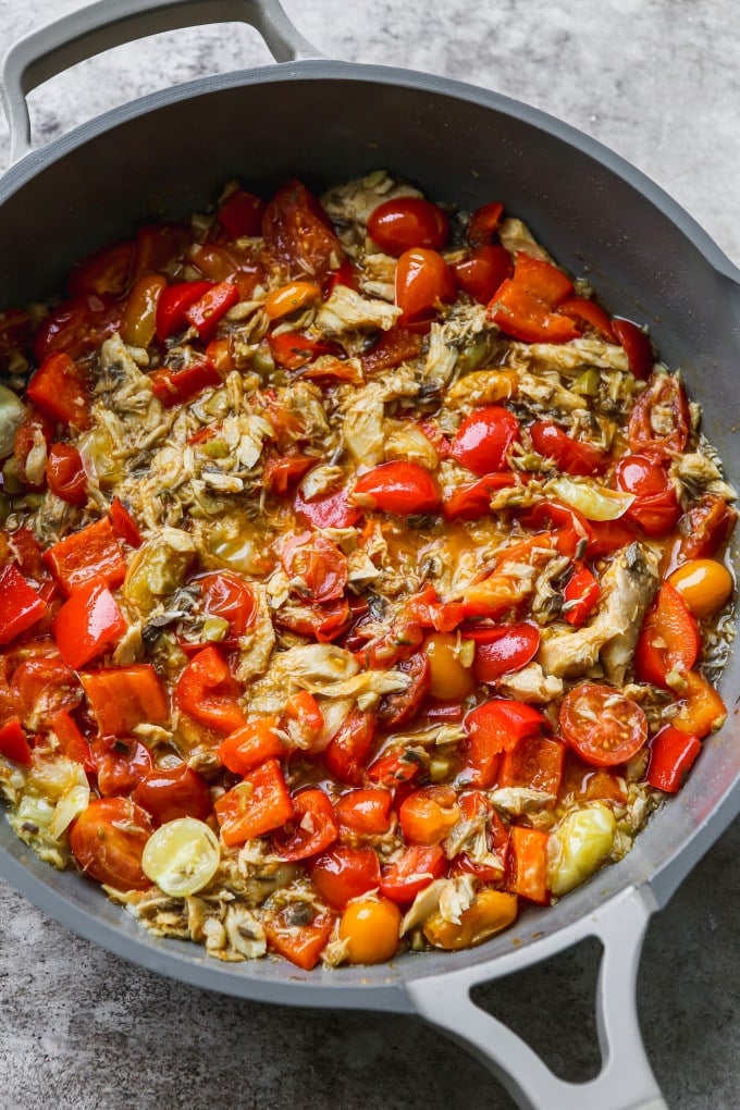 Cooked peppers, tomatoes, olives, garlic, and canned mackerel in a large pan.