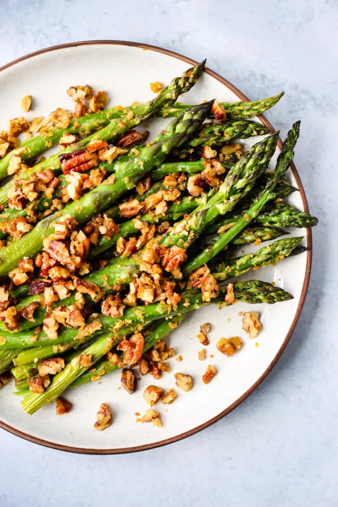 Roasted asparagus with chopped pecan parmesan on a white plate