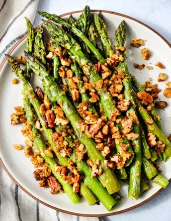 Roasted asparagus with chopped pecan parmesan on a white plate with a stripped dish towel