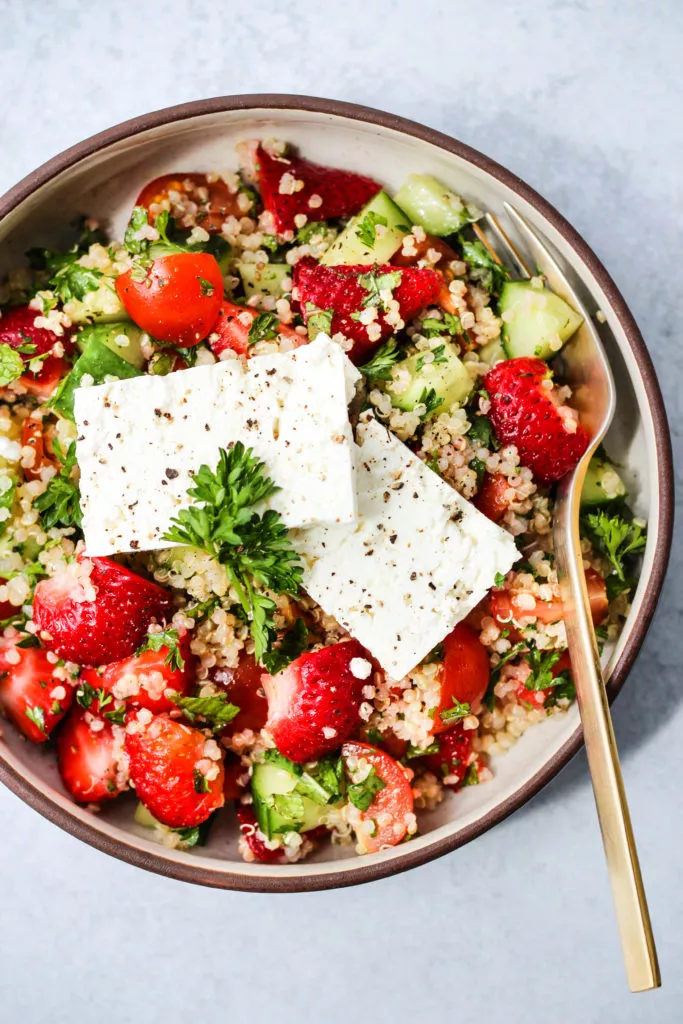 Overhead photo of small bowl with strawberry quinoa salad inside and 2 pieces of feta cheese on top.