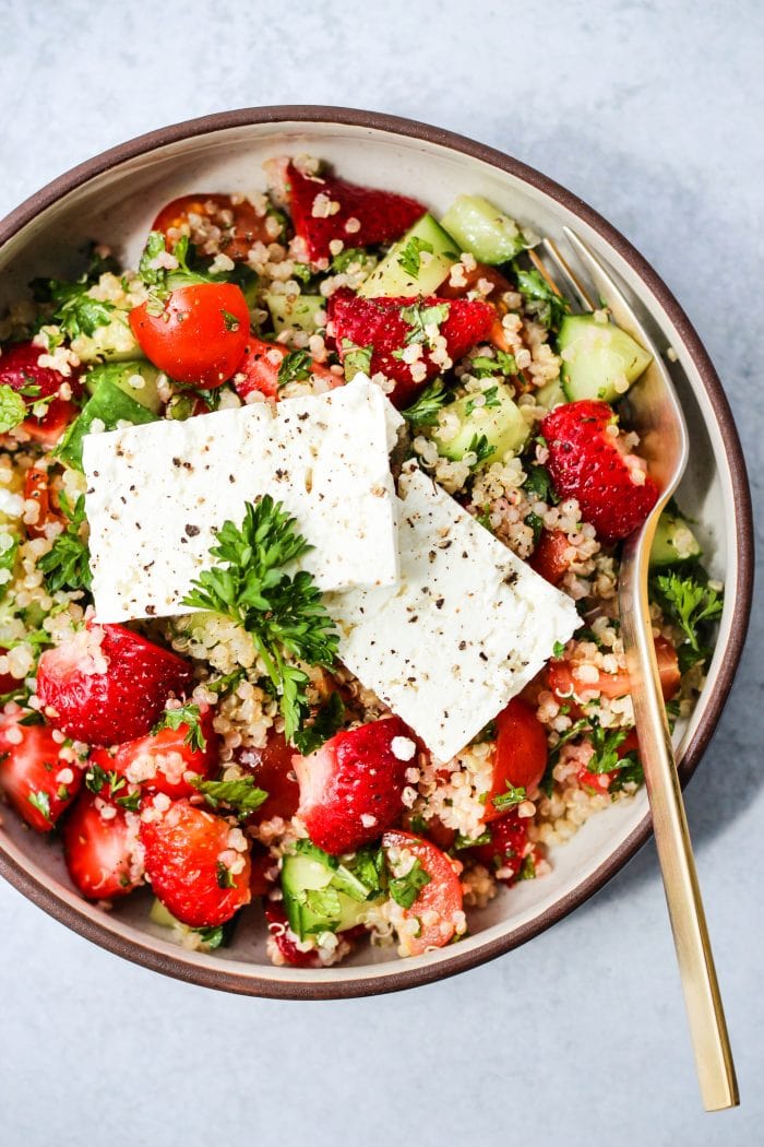 small bowl with strawberry quinoa tabbouleh salad and 2 pieces of feta cheese and gold fork