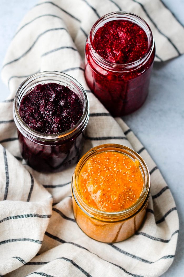 raspberry, blueberry, and apricot chia jam in three glass jars with striped towel