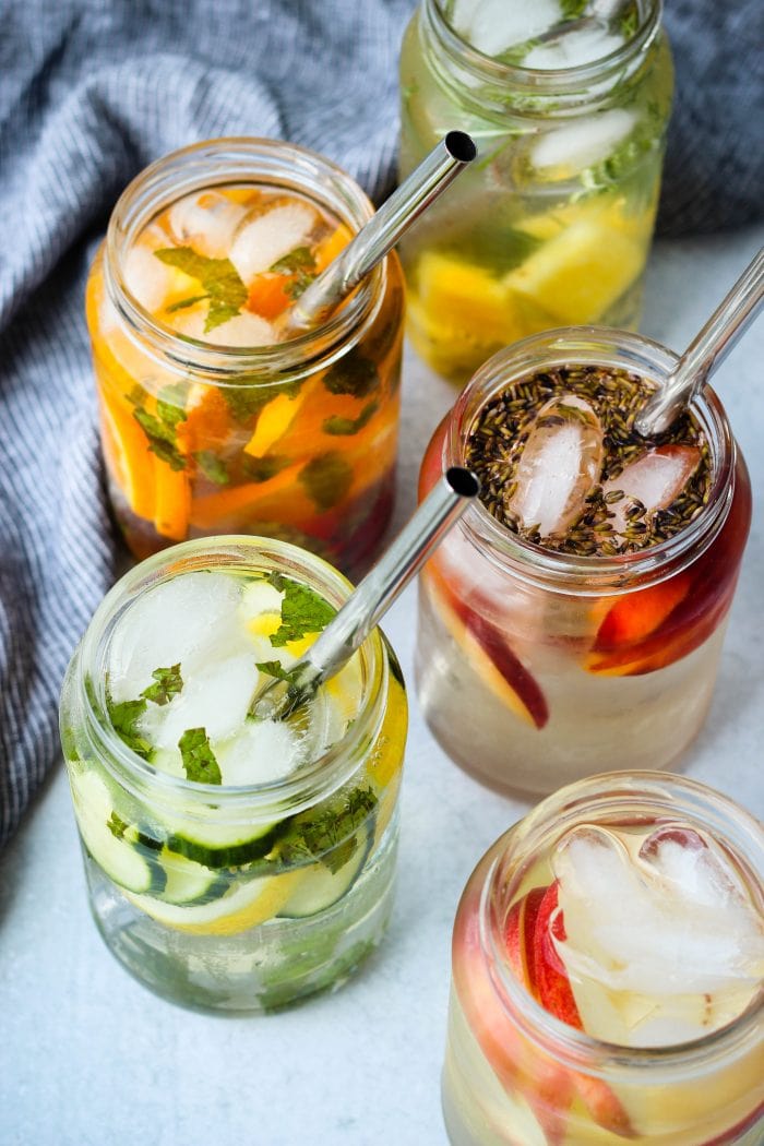 5 glass jars with fruit-infused water and metal straws