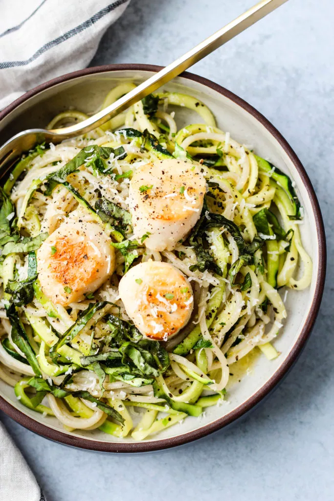 pan seared scallops and zucchini noodle pasta in a white and brown bowl