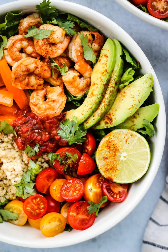 taco salad bowl with romaine lettuce, shrimp, avocado, bell peppers, tomatoes, quinoa, lime, cilantro
