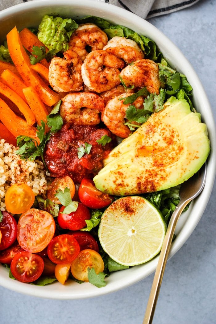 taco salad bowl with romaine lettuce, shrimp, avocado, bell peppers, tomatoes, quinoa, lime, cilantro