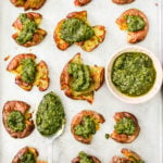 smashed red potatoes topped with pesto on baking sheet with bowl and spoon