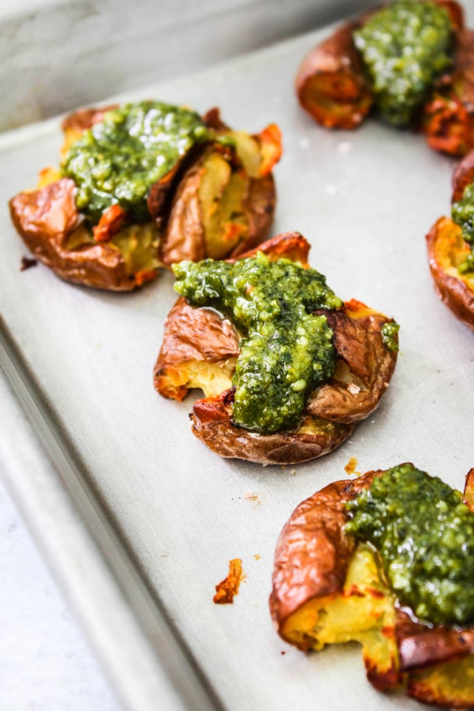 Closeup photo of 3 red smashed potatoes topped with pesto on a baking sheet.