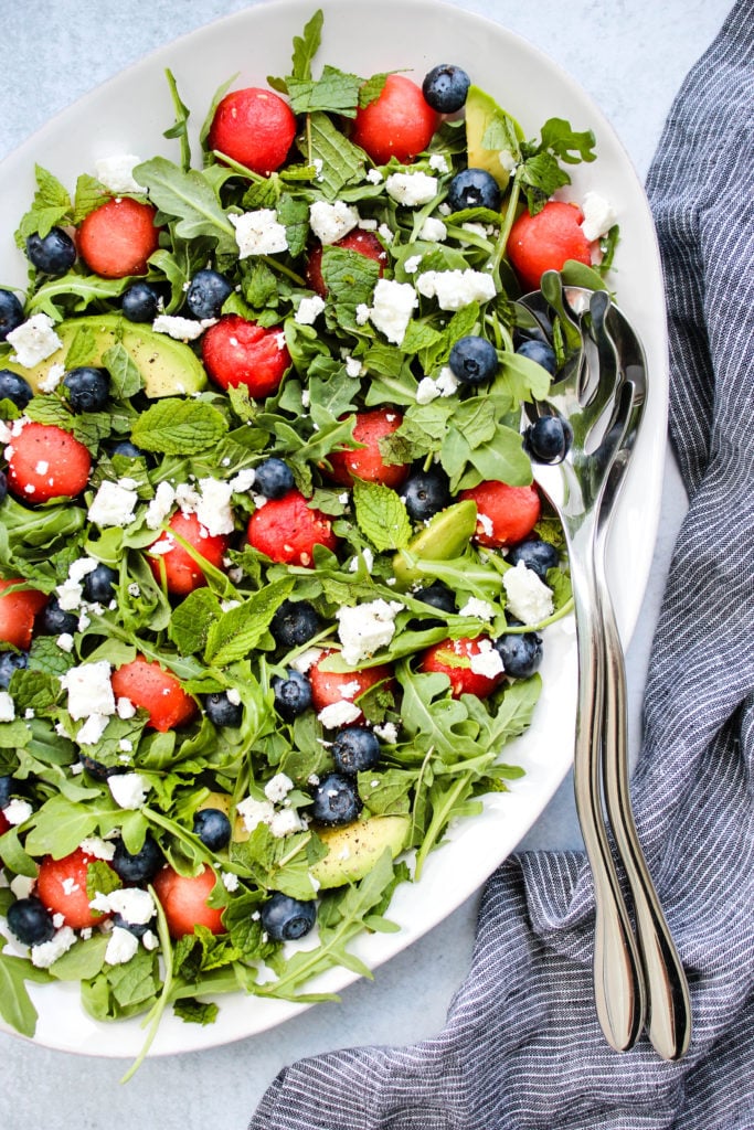 salad with arugula, watermelon, feta, blueberries, avocado on white plate