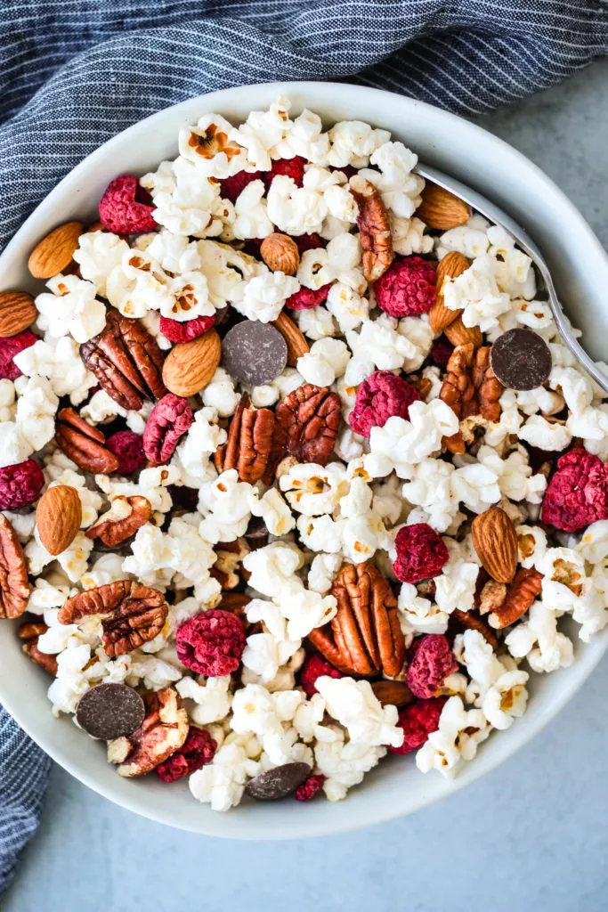 homemade trail mix with popcorn, chocolate chips, pecans, and almonds in a white bowl