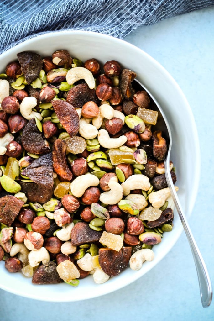 homemade trail mix with dried apricots, ginger, pistachios, cashews, and hazelnuts in a white bowl