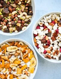 three white bowls of different homemade trail mix combinations