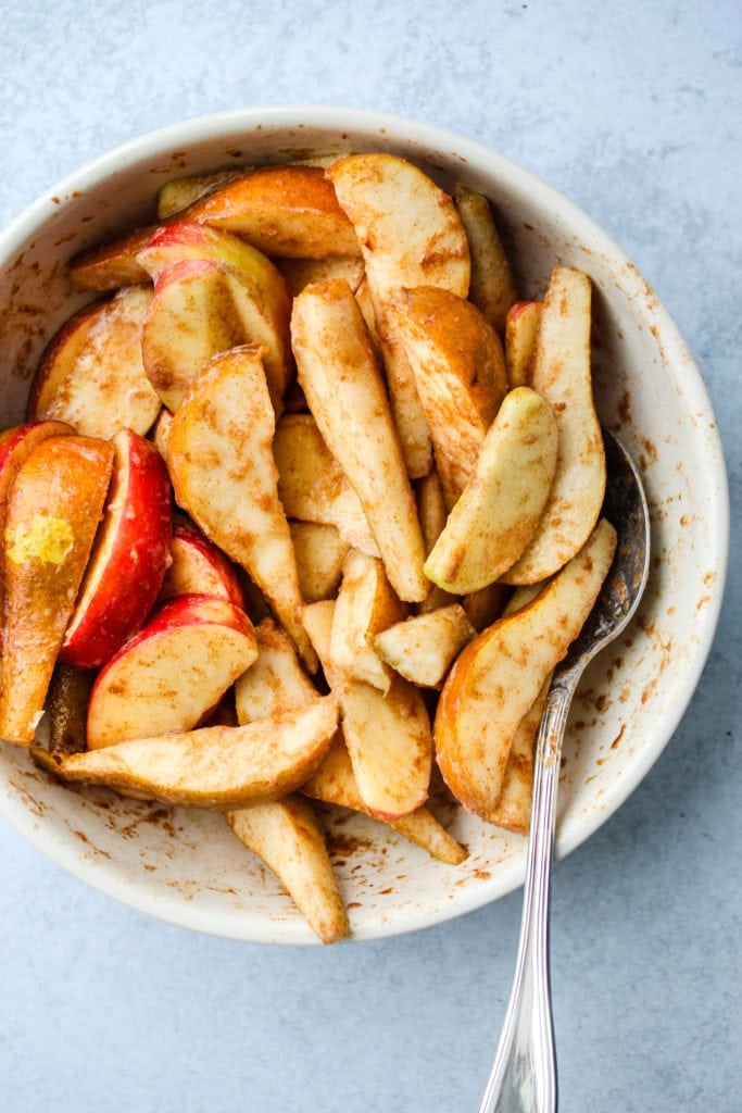 apple and pear slices tossed in spices in white mixing bowl