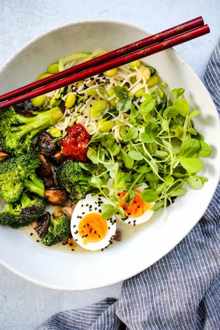homemade miso ramen noodle soup with broccoli, mushrooms, eggs, and microgreens in white bowl