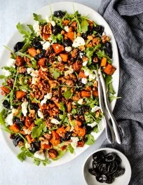 warm prune salad on white plate with arugula, sweet potatoes, goat cheese, and toasted walnuts