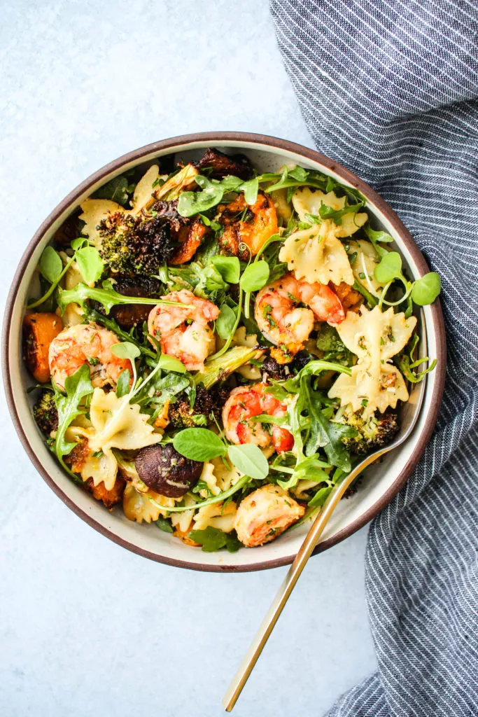 winter pasta salad with roasted butternut squash, mushrooms, broccoli, arugula, and shrimp in a bowl