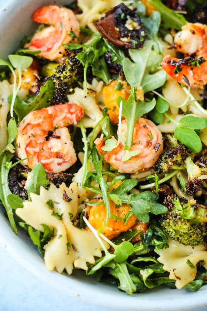 winter pasta salad with roasted butternut squash, mushrooms, broccoli, arugula, and shrimp in a bowl