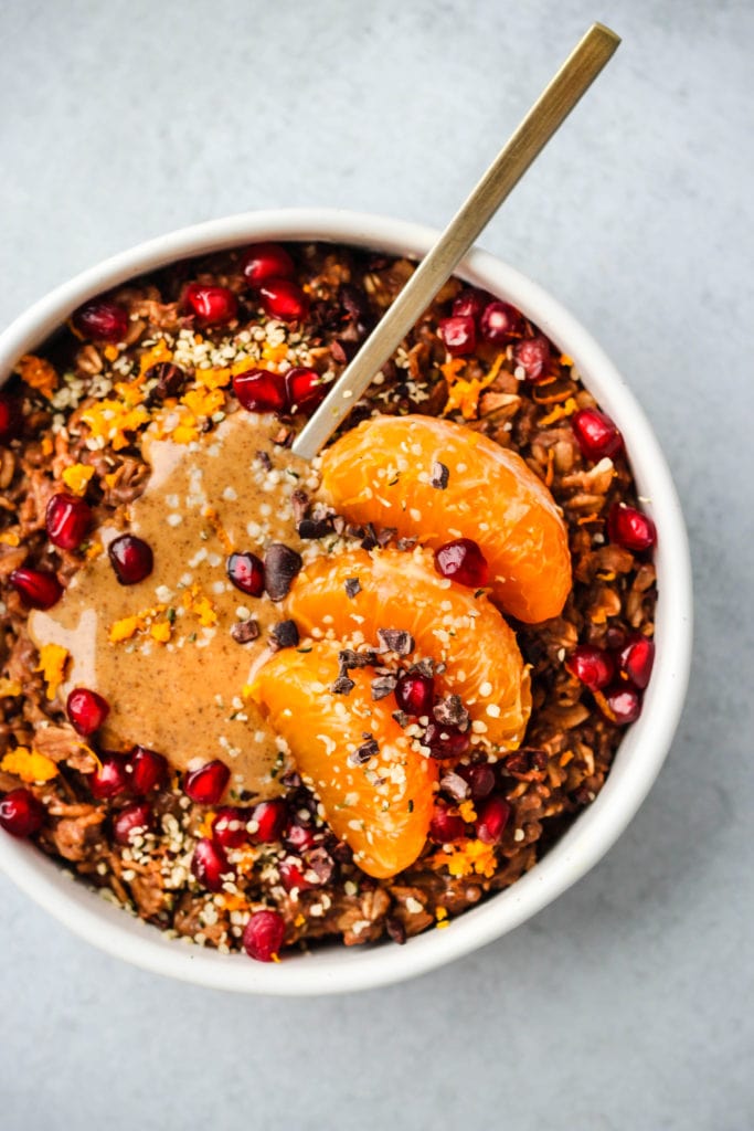 chocolate oatmeal topped with orange slices, pomegranates, and nut butter in bowl