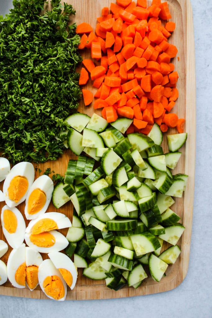 chopped parsley, carrots, cucumber, and hard boiled eggs on a wooden board
