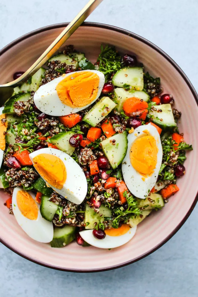 chopped quinoa salad with cucumbers, carrots, parsley, pomegranates, hard boiled eggs in pink bowl