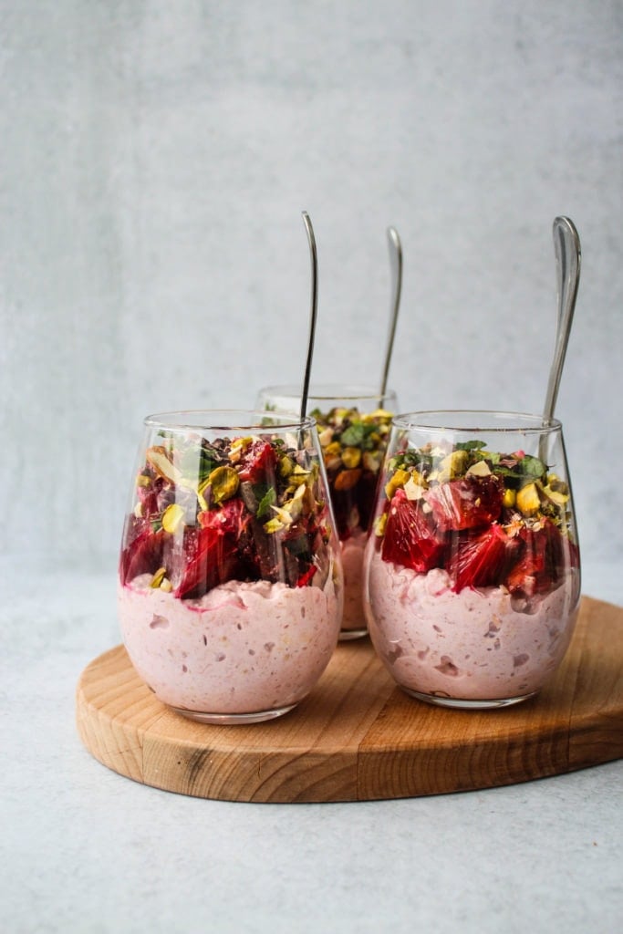 three glass jars of bircher muesli topped with blood oranges and nuts