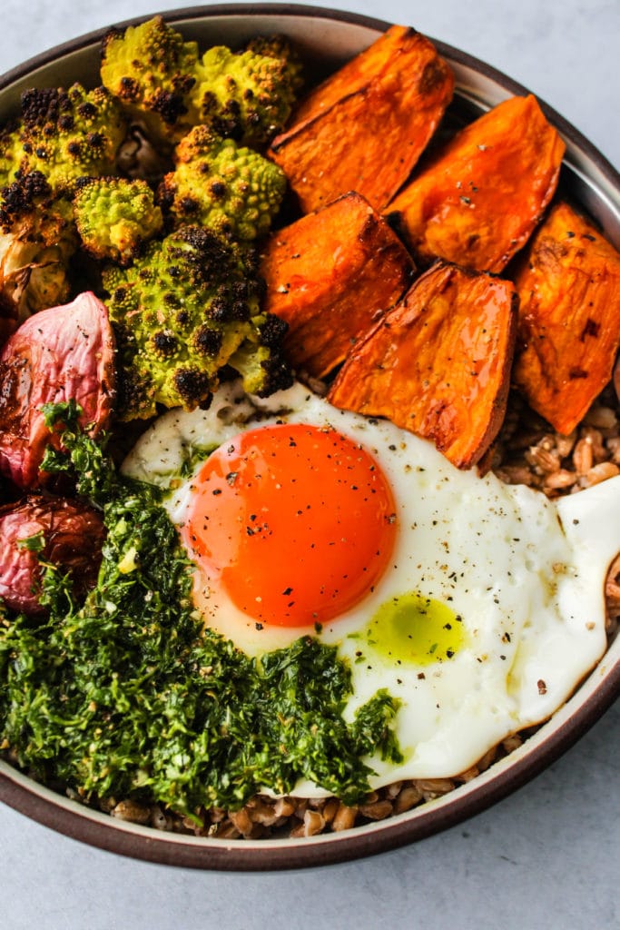 grain bowl with roasted sweet potatoes, romanesco, radishes, chimichurri sauce, and a fried egg