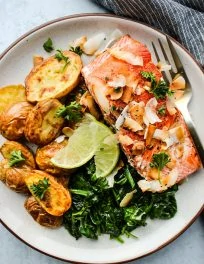 white plate with salmon fillet, potatoes, spinach, coconut, and lime