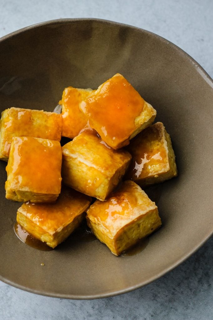 crispy baked tofu cubes topped with maple miso sauce in brown bowl