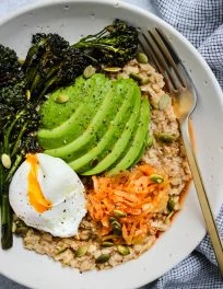 overhead shot of savoury oatmeal with poached egg, kimchi, avocado in white bowl