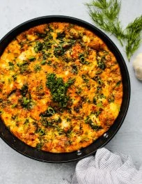frittata in skillet with spinach, feta cheese, and herbs