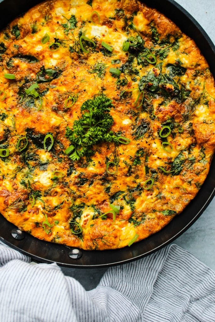 close up frittata in skillet with spinach, feta cheese, and herbs
