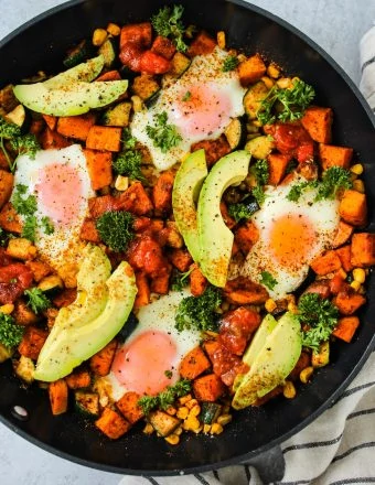 overhead shot of black skillet with sweet potatoes, corn, zucchini, eggs, and avocado slices