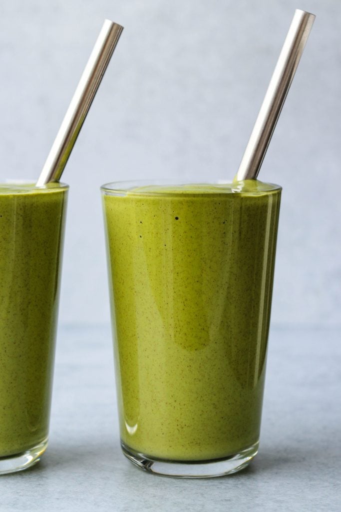 close up side shot of green smoothie in glass jar and metal straw