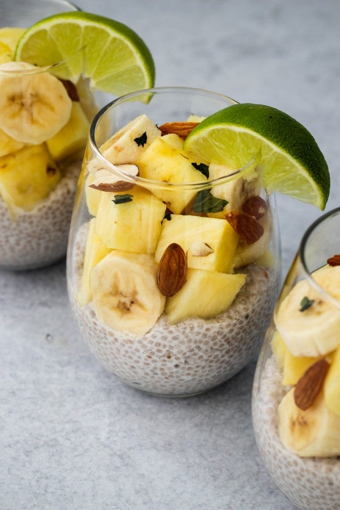 3 glass jars with coconut chia pudding, banana and pineapple slices, chopped almonds and lime