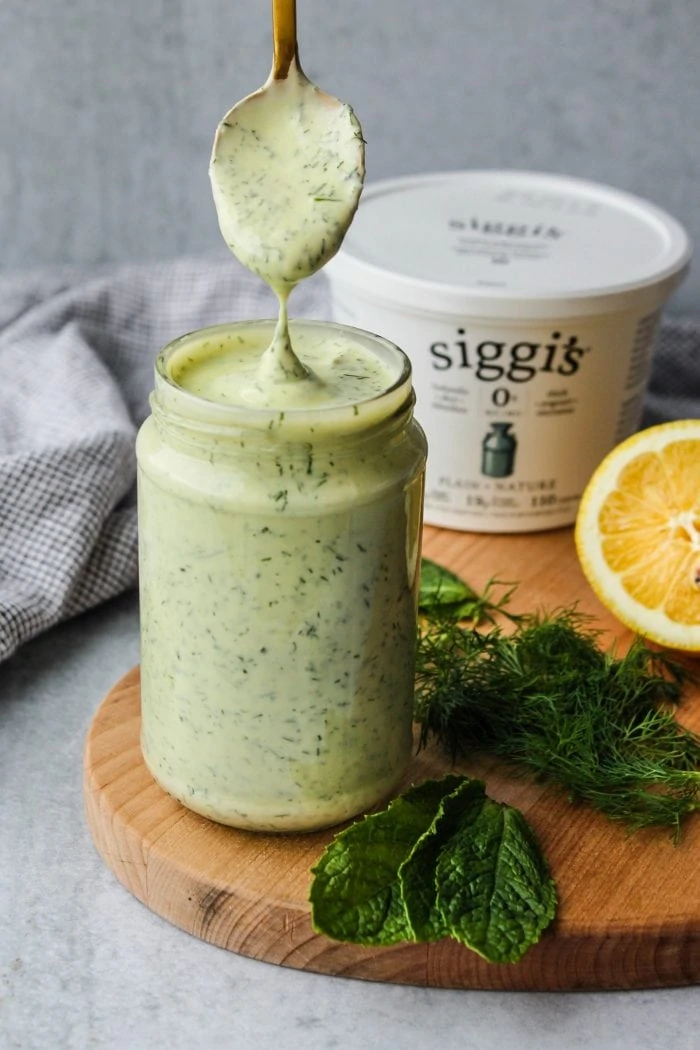 spoon dipping into glass jar with herbed siggis yogurt salad dressing